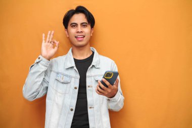 Elinde akıllı telefon tutan Asyalı adam gülümsüyor. Sarı arka planda mükemmel bir sembol. Akıllı telefon pozu veren Asyalı bir adam..