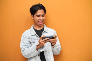 Mobil video oyunu uygulamasında akıllı telefon oyunu oynayan heyecanlı Asyalı genç oyuncu ya da sarı arka planda izole edilmiş dijital video akışını izleyen.