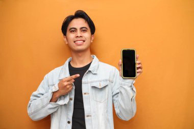 Mutlu Asyalı genç adam cep telefonu uygulama reklamları sunan sarı arka planda izole edilmiş büyük boş telefon şablonu ekranını işaret ederek akıllı telefon gösteriyor..