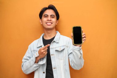 Mutlu Asyalı genç adam cep telefonu uygulama reklamları sunan sarı arka planda izole edilmiş büyük boş telefon şablonu ekranını işaret ederek akıllı telefon gösteriyor..