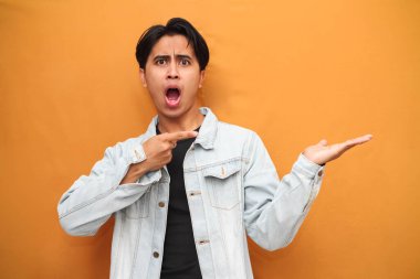 Vay canına, genç Asyalı adam avucunun içini işaret ediyor mutlu Asyalı genç adam sarı arka planda izole bir şekilde avucunun içine bakıyor..