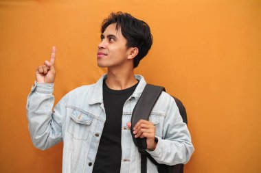 Sırt çantası taşıyan yakışıklı Asyalı öğrenci gülümserken boş bölgeyi işaret ediyor