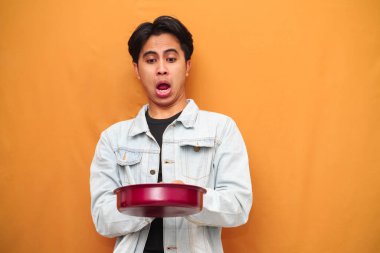 Uzaktaki sarı arka planda reklam için elinde tavayla Asyalı bir adamın şok olmuş portresi.