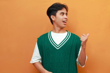 Yeşil kazaklı mutlu Asyalı adam, elini göstererek poz veriyor. Yan tarafı gösteren Asyalı adam.