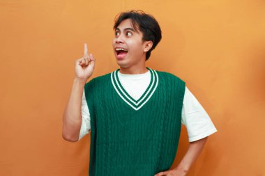 Yeşil kazaklı mutlu Asyalı adam, elini göstererek poz veriyor. Yan tarafı gösteren Asyalı adam.