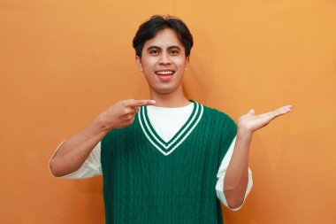 Yeşil kazaklı mutlu Asyalı adam, elini göstererek poz veriyor. Yan tarafı gösteren Asyalı adam.