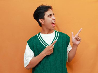 Yeşil kazaklı mutlu Asyalı adam, elini göstererek poz veriyor. Yan tarafı gösteren Asyalı adam.