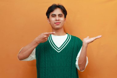 Yeşil kazaklı mutlu Asyalı adam, elini göstererek poz veriyor. Yan tarafı gösteren Asyalı adam.