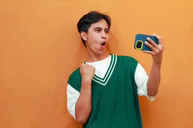 Yeşil kazaklı mutlu Asyalı adam oyun oynuyor ya da telefonda çığlıklar atıp zaferi ve başarıyı kutluyor.