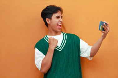 Yeşil kazaklı mutlu Asyalı adam oyun oynuyor ya da telefonda çığlıklar atıp zaferi ve başarıyı kutluyor.