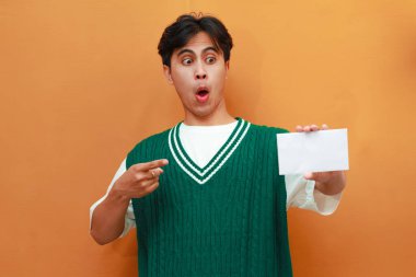 Mutlu Asyalı genç adam. Yeşil kazak giyiyor. Elinde reklam için beyaz bir kağıt tutuyor.