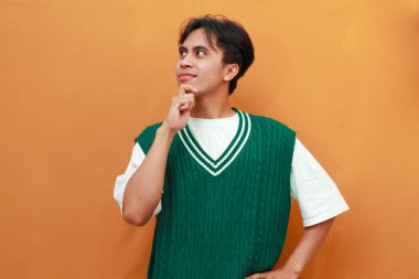 Yeşil kazaklı mutlu genç Asyalı adam turuncu arka planda izole edilmiş heyecanlı bir jest ile parlak bir fikir düşünüyor.