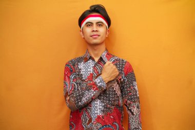 Batik tişörtlü Endonezyalı adam 17 Ağustos 'ta Endonezya Bağımsızlık Günü' nü kutluyor, elini kaldırıyor ve sarı arka planda izole edilmiş bir şekilde selamlıyor..