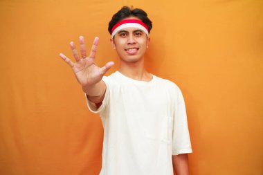 Mutlu bir Endonezyalı, sarı arka planda parmaklarıyla birden beşe kadar sayarak poz verir. Endonezya 'nın 17 Ağustos' taki bağımsızlık gününü kutlama konsepti.