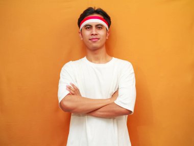 17 Ağustos 'ta Endonezya' nın Bağımsızlık Günü 'nü kutlayan gülümseyen Endonezyalı adam, sarı arka planda kollarını göğsüne dolayıp cesurca ve emin bir şekilde poz verdi..