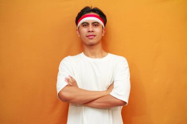 17 Ağustos 'ta Endonezya' nın Bağımsızlık Günü 'nü kutlayan gülümseyen Endonezyalı adam, sarı arka planda kollarını göğsüne dolayıp cesurca ve emin bir şekilde poz verdi..