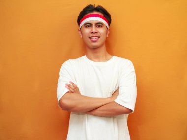 17 Ağustos 'ta Endonezya' nın Bağımsızlık Günü 'nü kutlayan gülümseyen Endonezyalı adam, sarı arka planda kollarını göğsüne dolayıp cesurca ve emin bir şekilde poz verdi..