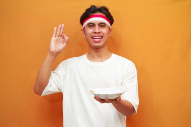 Sarı arka planda boş tabak tutan mutlu Endonezyalı adam.