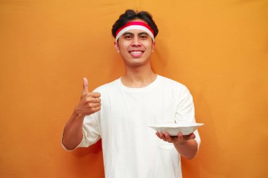 Sarı arka planda boş tabak tutan mutlu Endonezyalı adam.