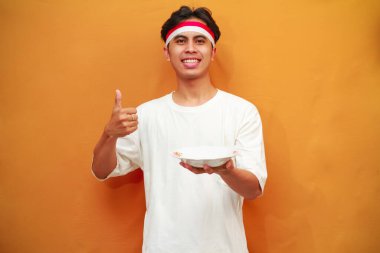 Sarı arka planda boş tabak tutan mutlu Endonezyalı adam.