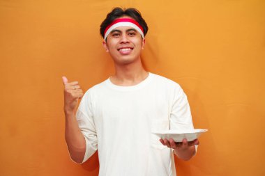 Sarı arka planda boş tabak tutan mutlu Endonezyalı adam.