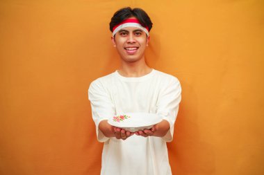 Sarı arka planda boş tabak tutan mutlu Endonezyalı adam.