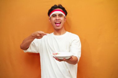 Sarı arka planda boş tabak tutan mutlu Endonezyalı adam.