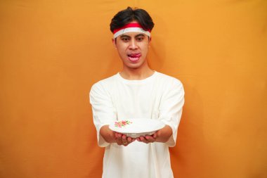 Sarı arka planda boş tabak tutan mutlu Endonezyalı adam.