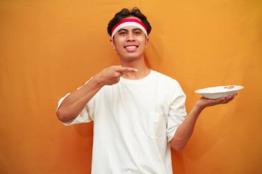 Sarı arka planda boş tabak tutan mutlu Endonezyalı adam.