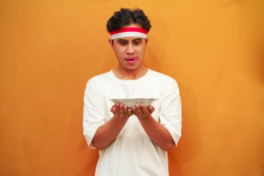 Sarı arka planda boş tabak tutan mutlu Endonezyalı adam.