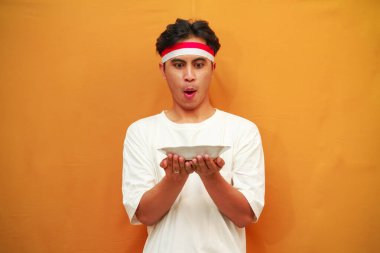 Sarı arka planda boş tabak tutan mutlu Endonezyalı adam.