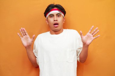 Endonezyalı adam 17 Ağustos 'ta Endonezya Bağımsızlık Günü' nü kutluyor, şaşırmış bir şekilde ellerini kaldırıyor ve sarı arka plandaki izole kameraya bakıyor..