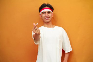 Gülümseyen Endonezyalı adam Endonezya Bağımsızlık Günü 'nü 17 Ağustos' ta kutluyor, elleriyle kalp işareti yapıyor. Sarı arka planda izole edilmiş Endonezya aşk sembolü.