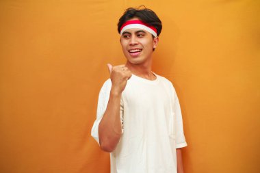 Mutlu bir Endonezyalı, sarı arka planda başparmağını yukarı kaldırarak poz verir. Endonezya 'nın 17 Ağustos' taki bağımsızlık gününü kutlama konsepti.