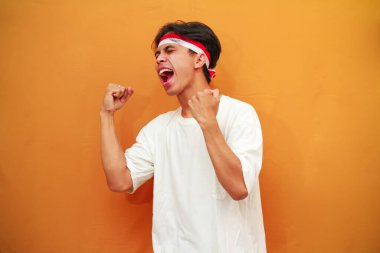 17 Ağustos 'ta Endonezya' nın bağımsızlığını kutlayan mutlu Endonezyalı adam sarı arka planda izole edilmiş zaferi haykırıyor ve kutluyor.