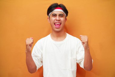 17 Ağustos 'ta Endonezya' nın bağımsızlığını kutlayan mutlu Endonezyalı adam sarı arka planda izole edilmiş zaferi haykırıyor ve kutluyor.