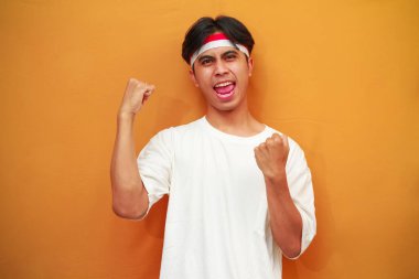 17 Ağustos 'ta Endonezya' nın bağımsızlığını kutlayan mutlu Endonezyalı adam sarı arka planda izole edilmiş zaferi haykırıyor ve kutluyor.