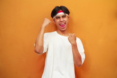 17 Ağustos 'ta Endonezya' nın bağımsızlığını kutlayan mutlu Endonezyalı adam sarı arka planda izole edilmiş zaferi haykırıyor ve kutluyor.