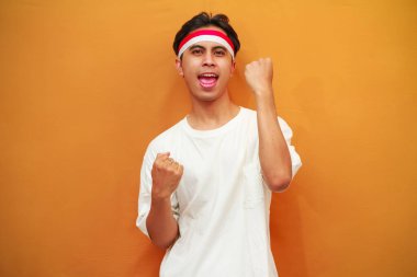 17 Ağustos 'ta Endonezya' nın bağımsızlığını kutlayan mutlu Endonezyalı adam sarı arka planda izole edilmiş zaferi haykırıyor ve kutluyor.