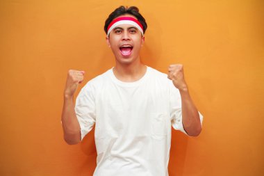 17 Ağustos 'ta Endonezya' nın bağımsızlığını kutlayan mutlu Endonezyalı adam sarı arka planda izole edilmiş zaferi haykırıyor ve kutluyor.