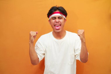 17 Ağustos 'ta Endonezya' nın bağımsızlığını kutlayan mutlu Endonezyalı adam sarı arka planda izole edilmiş zaferi haykırıyor ve kutluyor.