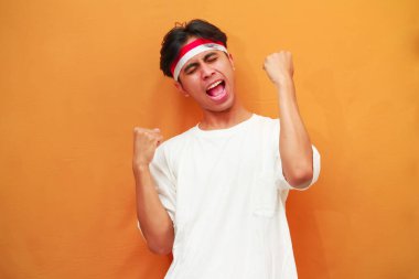 17 Ağustos 'ta Endonezya' nın bağımsızlığını kutlayan mutlu Endonezyalı adam sarı arka planda izole edilmiş zaferi haykırıyor ve kutluyor.