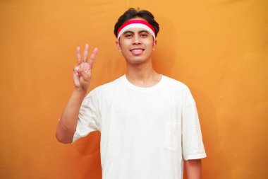 Gülümseyen Endonezyalı adam Endonezya Bağımsızlık Günü 'nü 17 Ağustos' ta kutluyor, elini kaldırıyor ve sarı arka planda parmakları izole edilmiş üç rakamı gösteriyor..