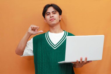 Yeşil kazaklı genç Asyalı adam elinde bilgisayarla gülümseyerek poz veriyor.