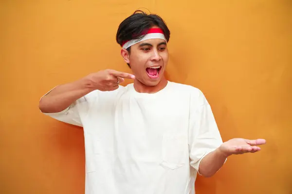 stock image happy Indonesian man celebrating Indonesian independence day on August 17th, wow excited face of Indonesian man celebrating Indonesian independence day while pointing with his finger to his open palm