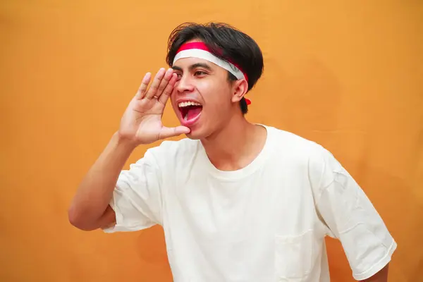 stock image Happy Indonesian man celebrating Indonesian independence day on August 17, scream sharing hot news about sales discount with hands near mouth isolated on yellow background.