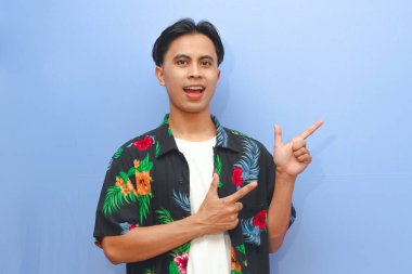 Plaj tişörtü giyen genç Asyalı adam boş telif alanını işaret ederek mutlu bir ifadeyle mavi arka planı izole etti.
