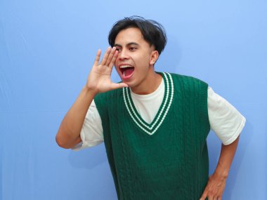 Mutlu, heyecanlı Asyalı bir adamın portresi indirimle ilgili sıcak haberleri paylaşıyor ve elleri ağızlarına yakın, mavi arka planda.