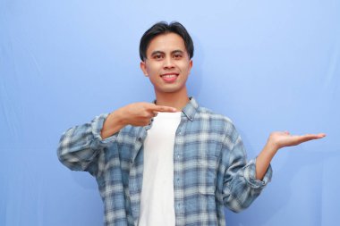 Çekici Asyalı bir adam gülümserken mavi arka planda açık avucunu işaret ediyor.