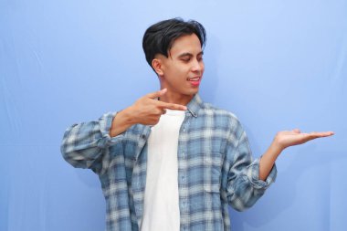 Çekici Asyalı bir adam gülümserken mavi arka planda açık avucunu işaret ediyor.